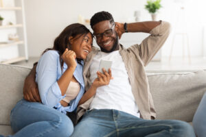 African american couple sitting on couch using cellphone